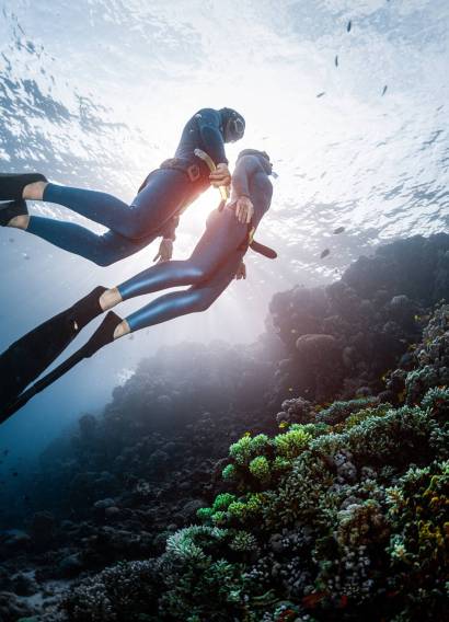 Two freedivers swim over the vivid coral reef in a tropical sea during their recreational freedive session